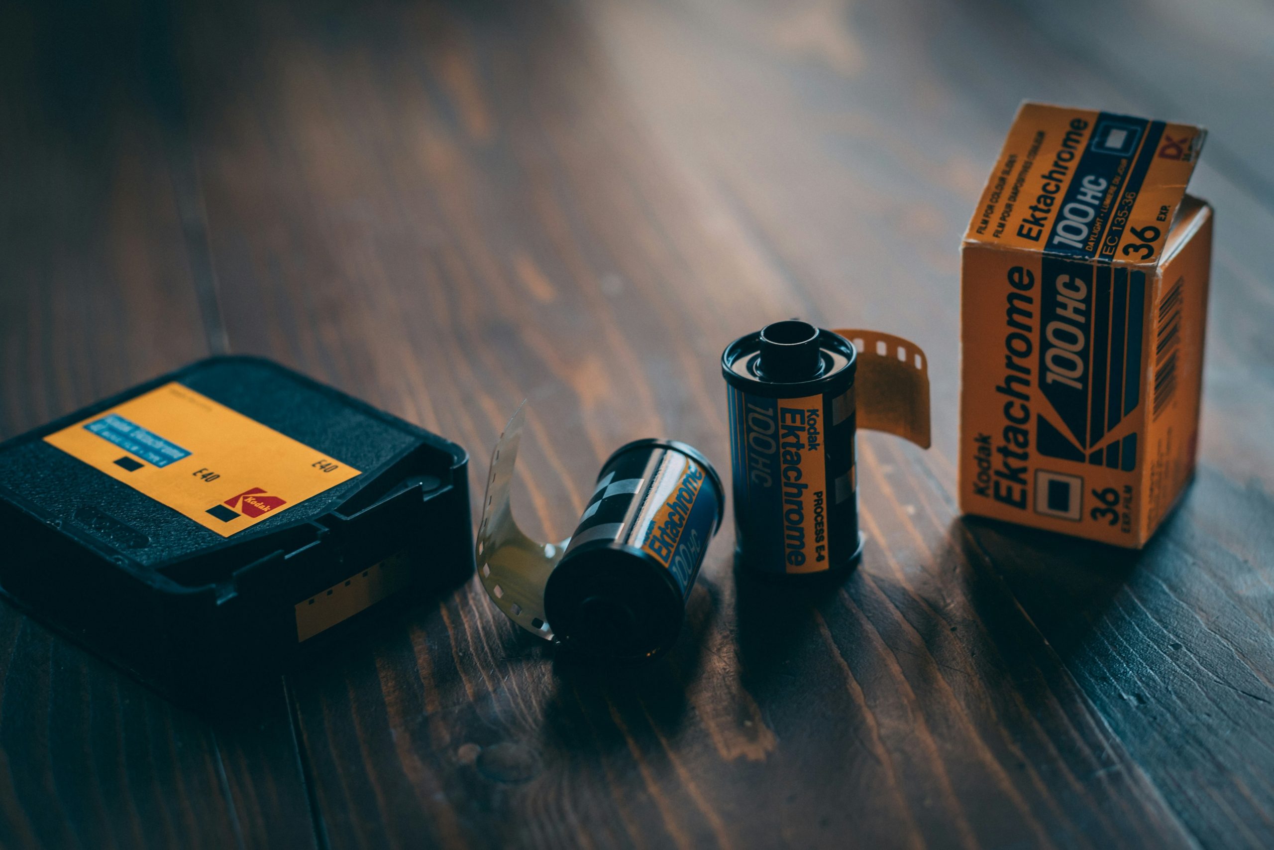 Kodak Ektachrome 100HC film canisters and packaging on wooden surface, related to photography and film development.